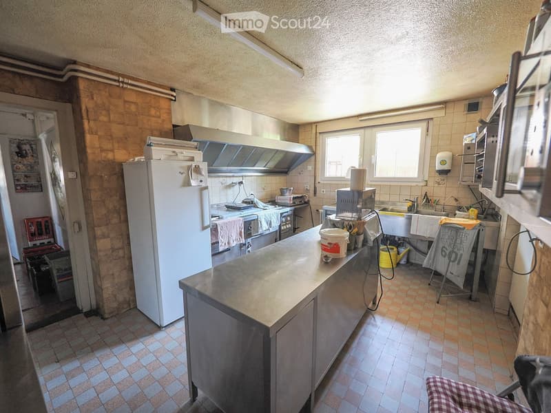 Commercial kitchen with stainless steel counter, refrigerator, sink, microwave, oven, and various utensils.