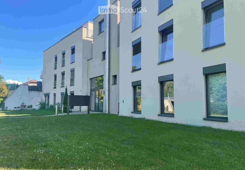 Modern multi-story building with light-colored facade, large windows, and a well-maintained lawn in front.