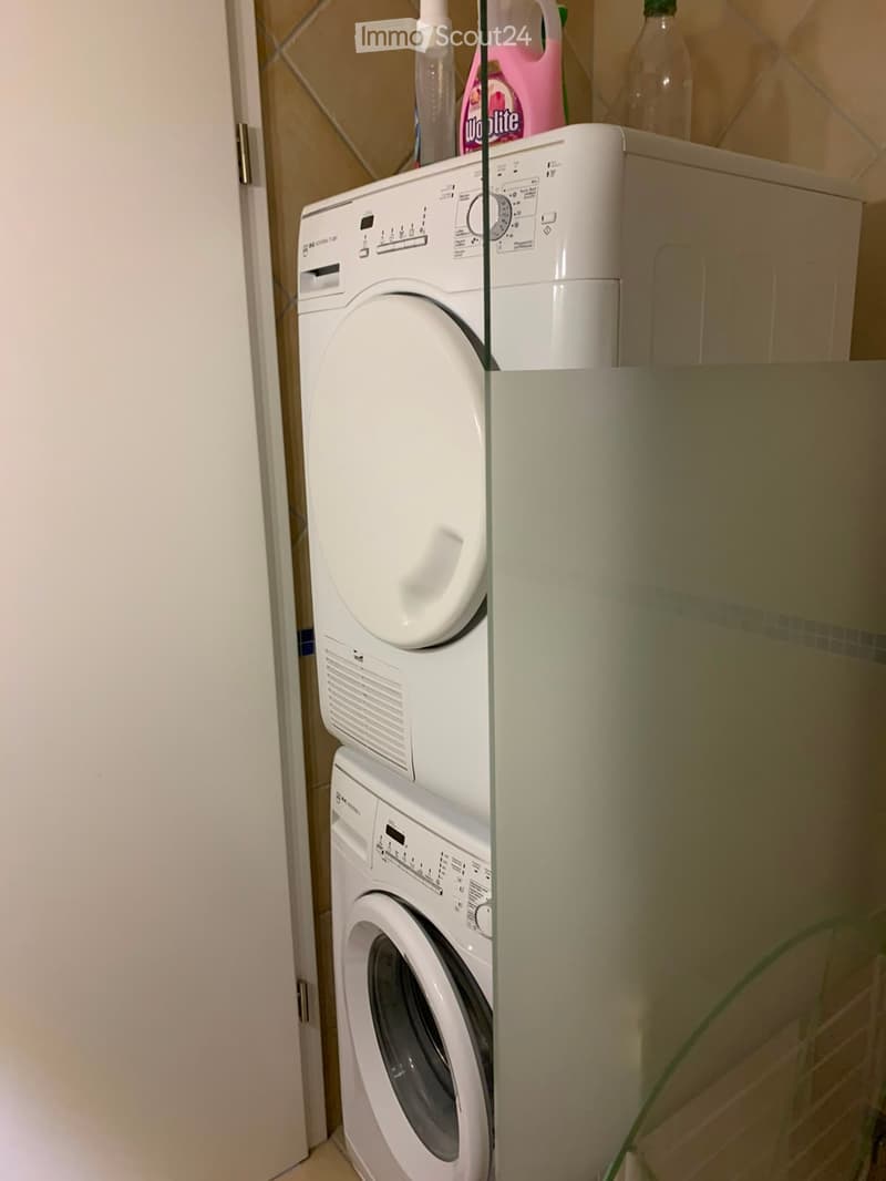 A compact bathroom with a stacked washing machine and dishwasher unit, featuring tiled walls and a small shelf holding cleaning supplies.