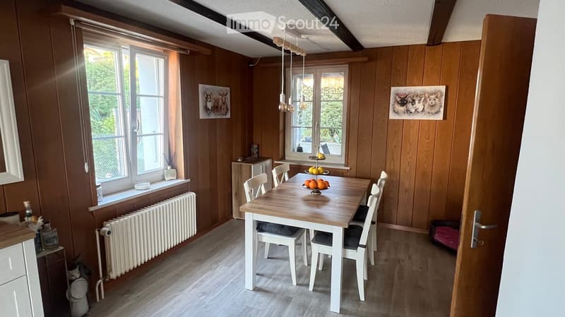 Dining area with wooden walls, a dining table with chairs, a fruit bowl, and artwork on the walls.