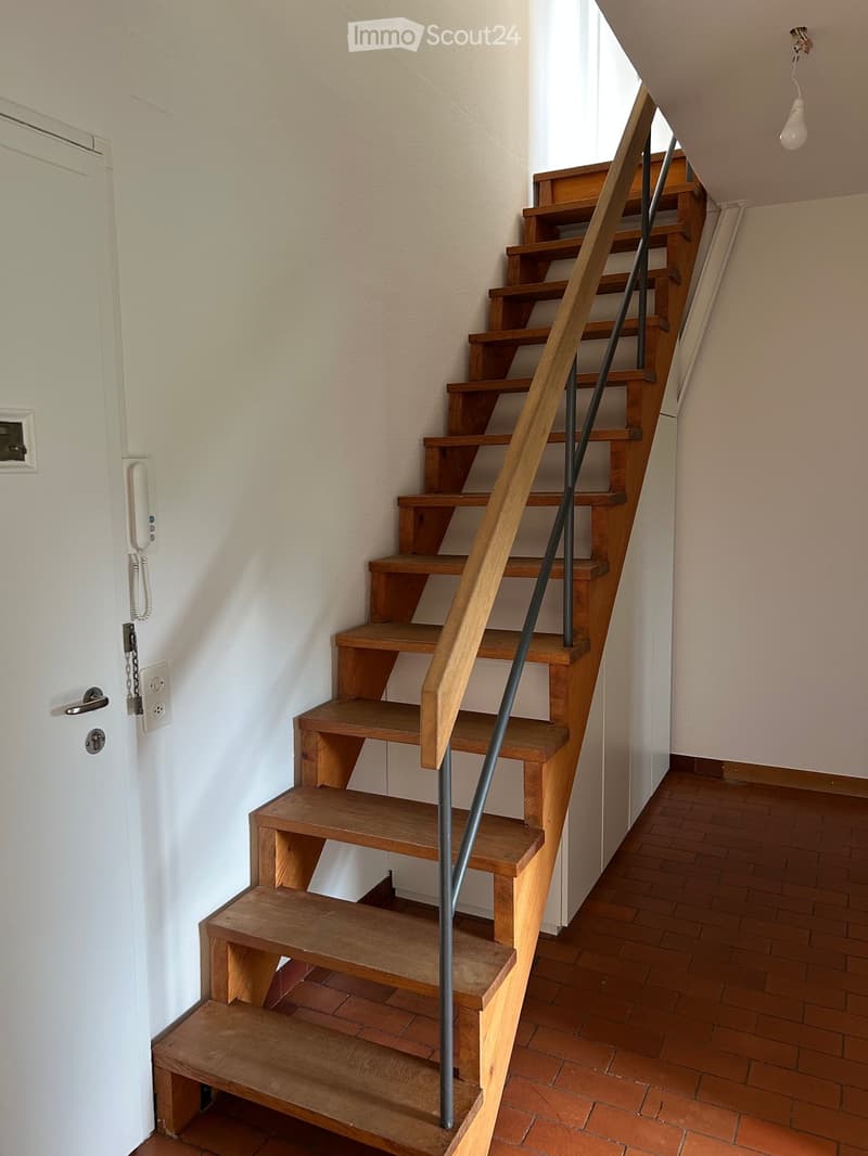 Wooden staircase with metal railing, wooden steps, and a light fixture on the wall.