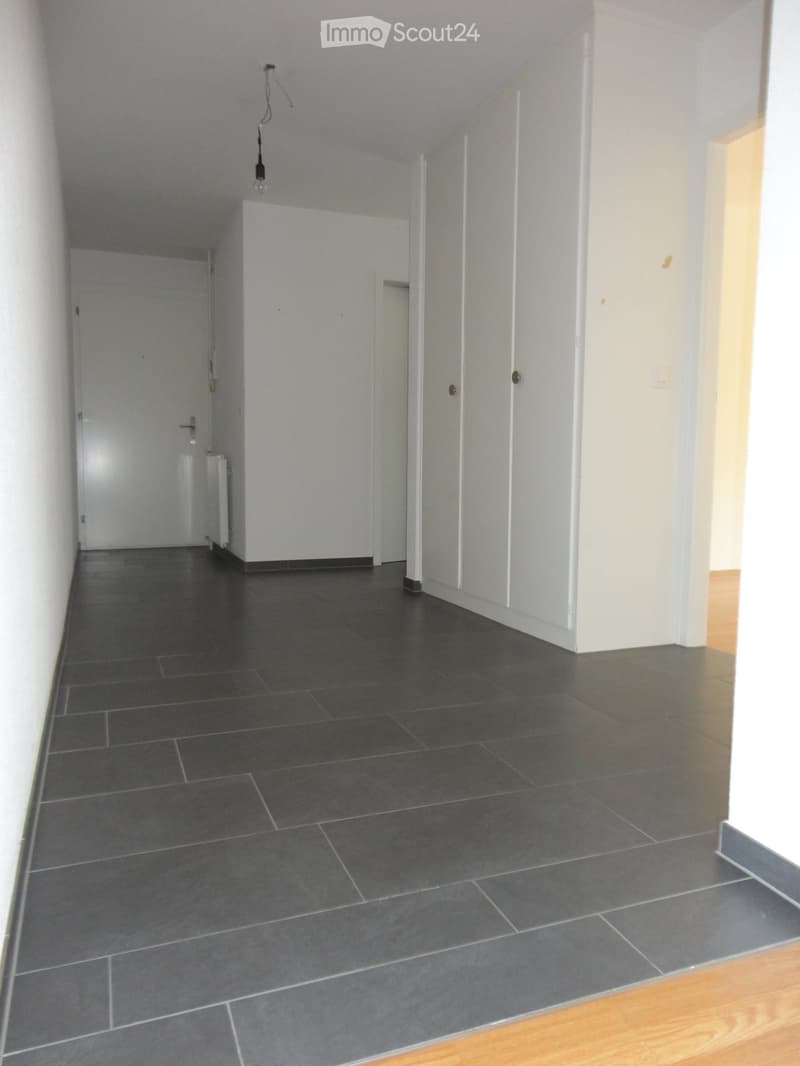 Empty hallway with dark grey tiled floor and white walls, featuring several doors and a radiator on the left side.