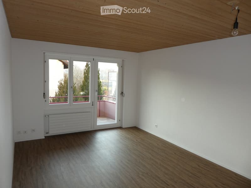 Empty room with wooden flooring, white walls, large window, and sliding glass door leading to a balcony.