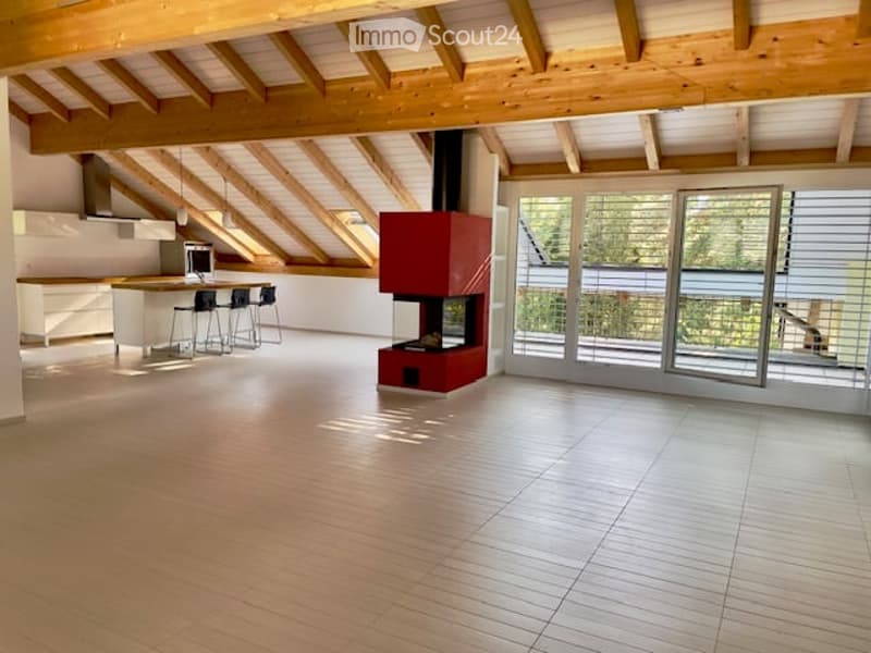 Open-plan living and kitchen area with exposed wooden beams, a modern fireplace, and large sliding glass doors leading to a balcony.