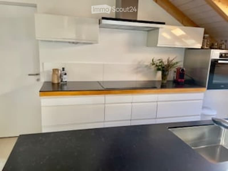Modern kitchen with white cabinets, black countertop, stainless steel sink and oven, and a range hood. Decorative items on the counter.