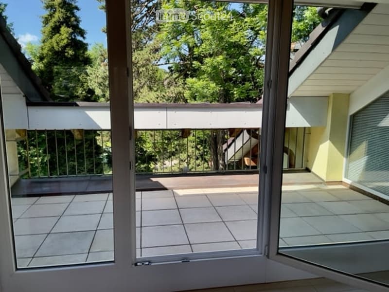 Balcony with tiled floor, metal railing, and view of green trees and neighboring building.