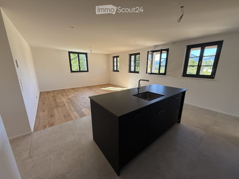 Modern kitchen with a black island, wooden flooring, and large windows offering a scenic view.