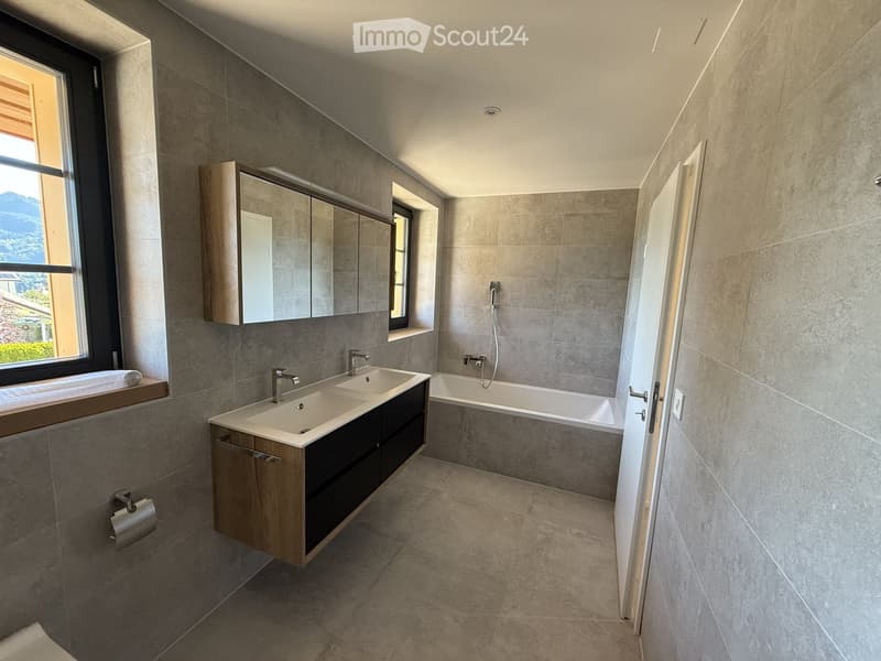 Modern bathroom with double sink, bathtub, large mirror, and wooden cabinet.