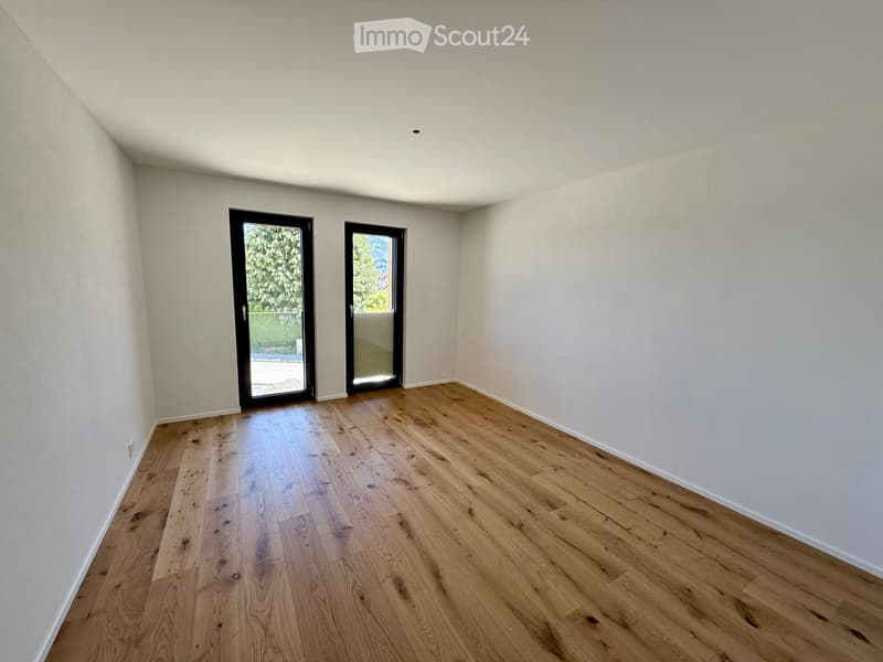 Empty room with light wooden flooring and white walls, featuring two large black-framed glass doors leading outside.