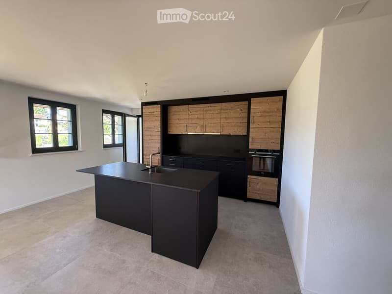Modern kitchen with a black island, wooden cabinets, and stainless steel appliances.
