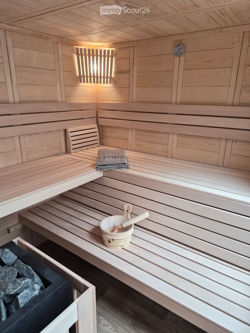 Wooden sauna interior with benches, a wooden bucket with a wooden spoon, and a towel on the bench.