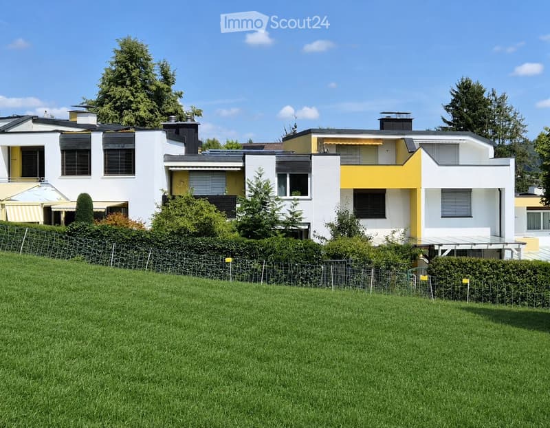 Modern two-story house with white and yellow exterior, multiple windows, and a well-maintained lawn in front.
