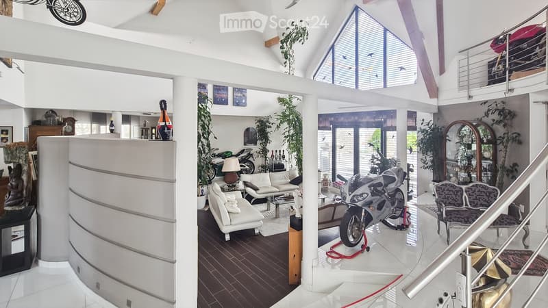Open-concept living space with high ceilings, large windows, and modern decor. Features a white sofa, coffee table, chairs, table lamp, and a motorcycle on display. Additional decor includes vases, a clock, and artwork.