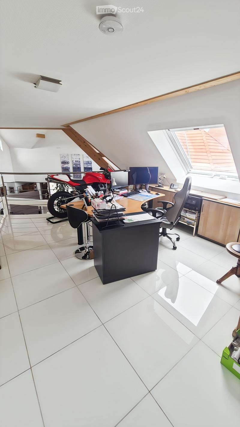 Office space with white tiled floor, slanted ceiling, large window, desk with computer, office chair, motorcycle, and cabinet.