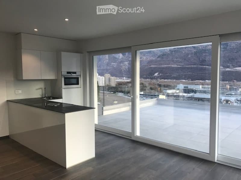 Modern kitchen with white cabinets, a central island, and large floor-to-ceiling windows offering a scenic mountain view.