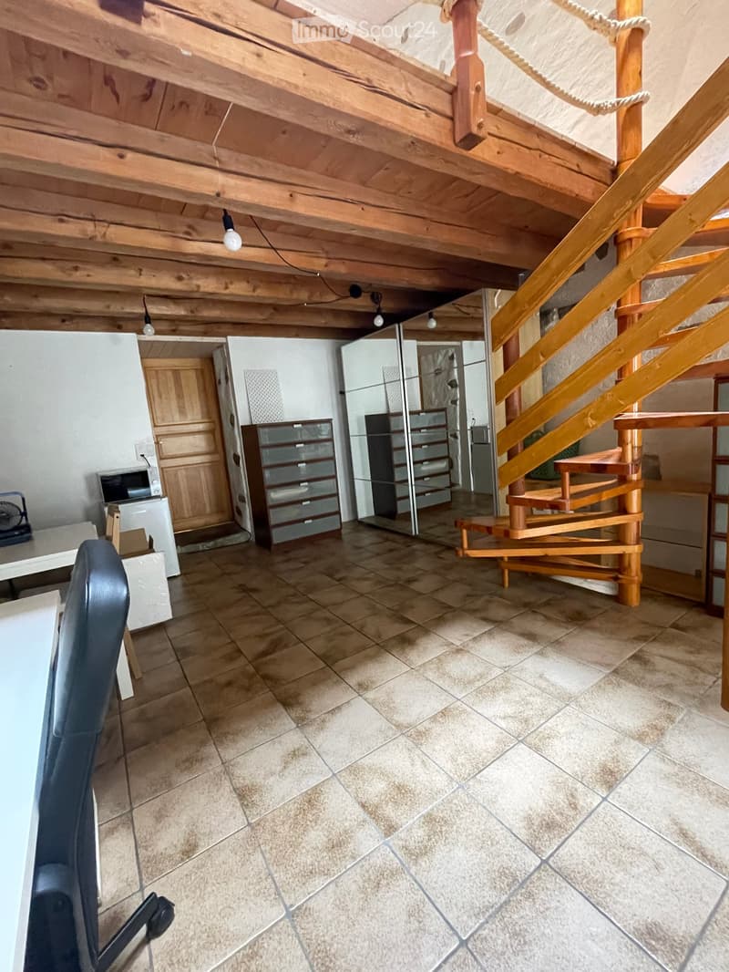 The room features a tiled floor, a wooden staircase leading to an attic space, a chair, a table, a refrigerator, a microwave, and a cabinet.