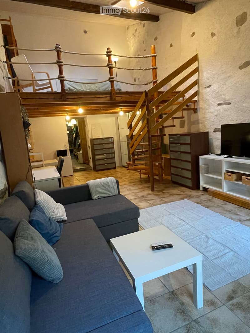 A cozy living space with a blue sofa, white coffee table, TV stand, and a lofted bedroom area accessible by wooden stairs.