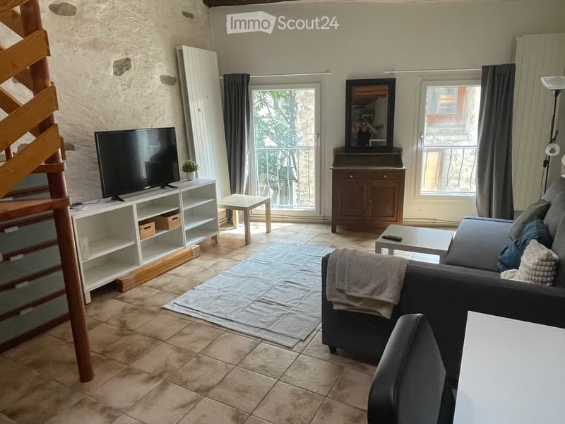 Living room with tiled floor, large windows, grey sofa, coffee table, TV stand, mirror, and cabinet.