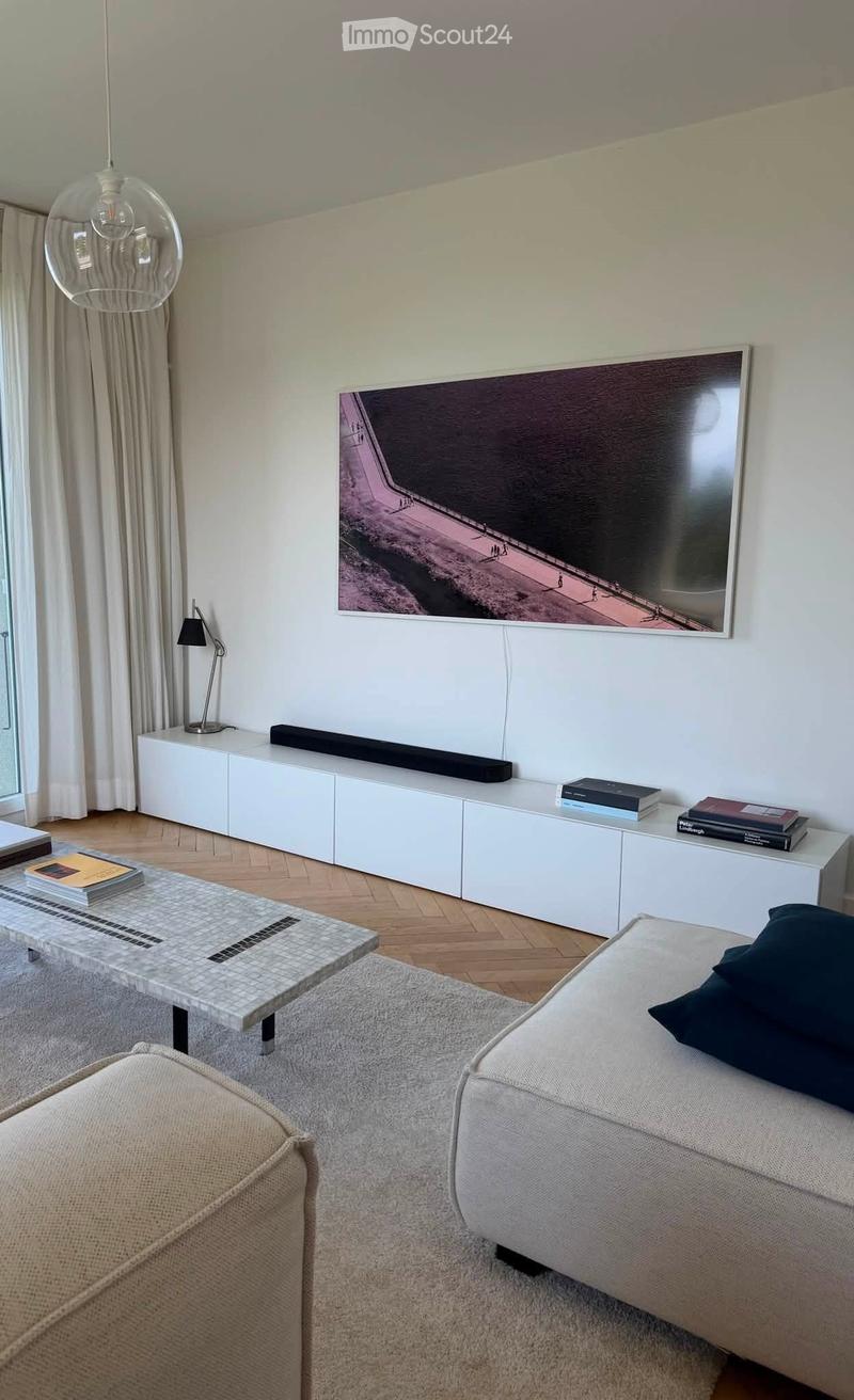 Modern living room with a grey sofa, coffee table, side table, books, picture frame, floor lamp, and cabinet.