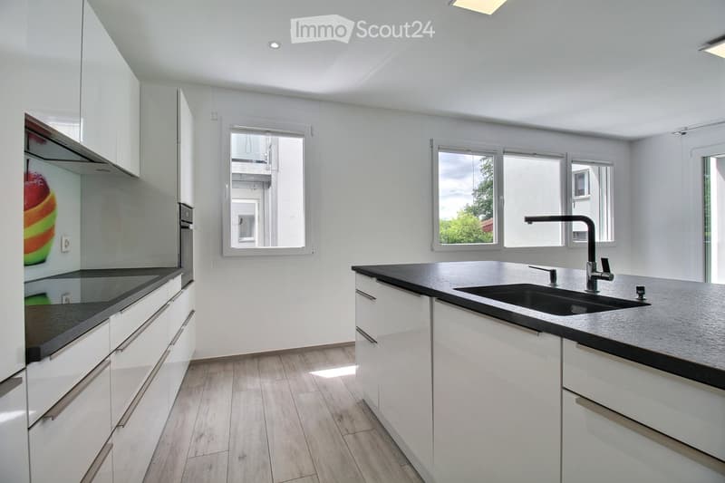Modern kitchen with white cabinets, black countertops, and a central island with a sink and faucet. Large windows provide natural light.