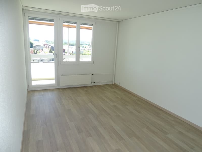 Empty room with wooden floor, sliding glass doors to balcony, white walls, view of the city.
