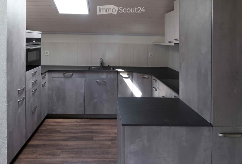 Modern kitchen with grey cabinets, black countertops, and a central island. Features a sink, oven, and ample storage space.