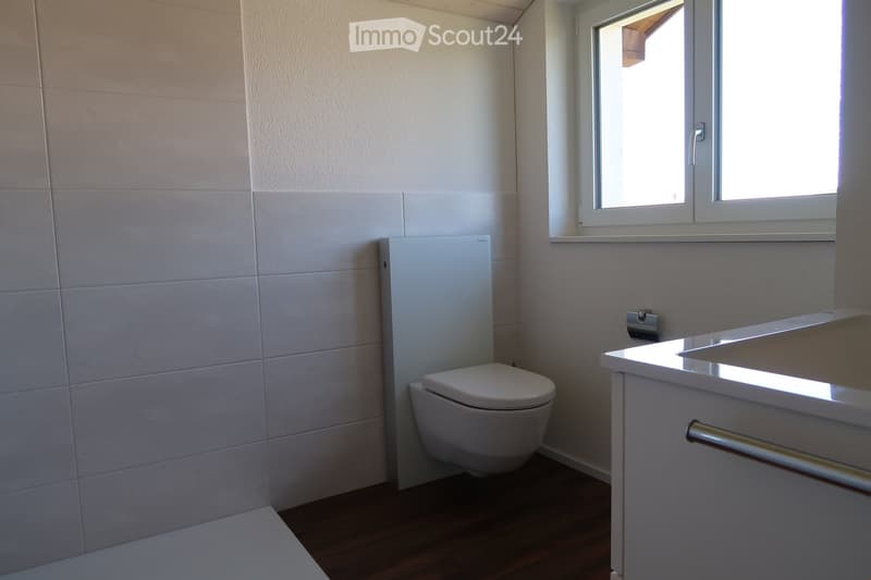 Modern bathroom with white tiled walls, a toilet, a sink with a cabinet, and a window letting in natural light.
