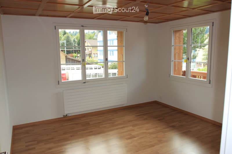 Empty room with wooden flooring, white walls, large windows, and a radiator. No furniture or equipment present.