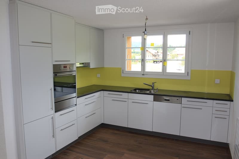 Modern kitchen with white cabinets, stainless steel appliances, dark green countertops, and wooden flooring.