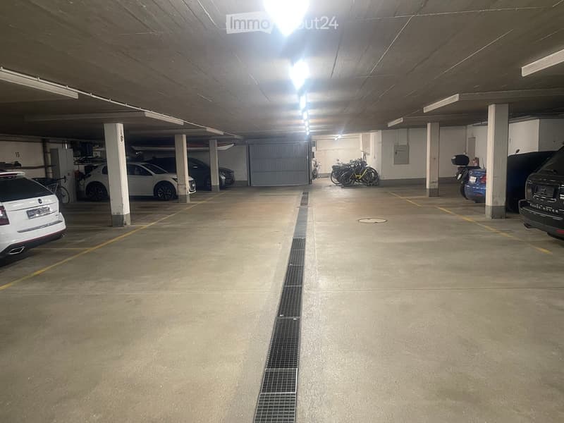 Underground parking area with several parked cars, bicycles, and pillars supporting the ceiling.