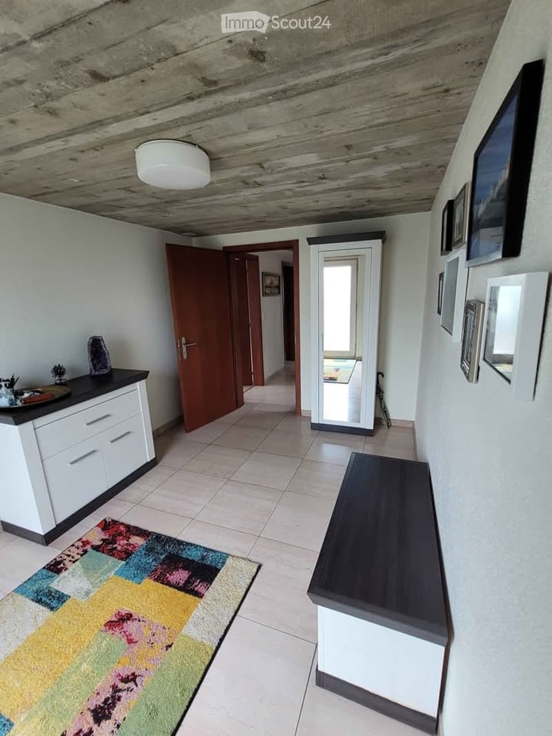 Hallway with a colorful rug, a bench, a mirror, a small cabinet, and picture frames on the wall.