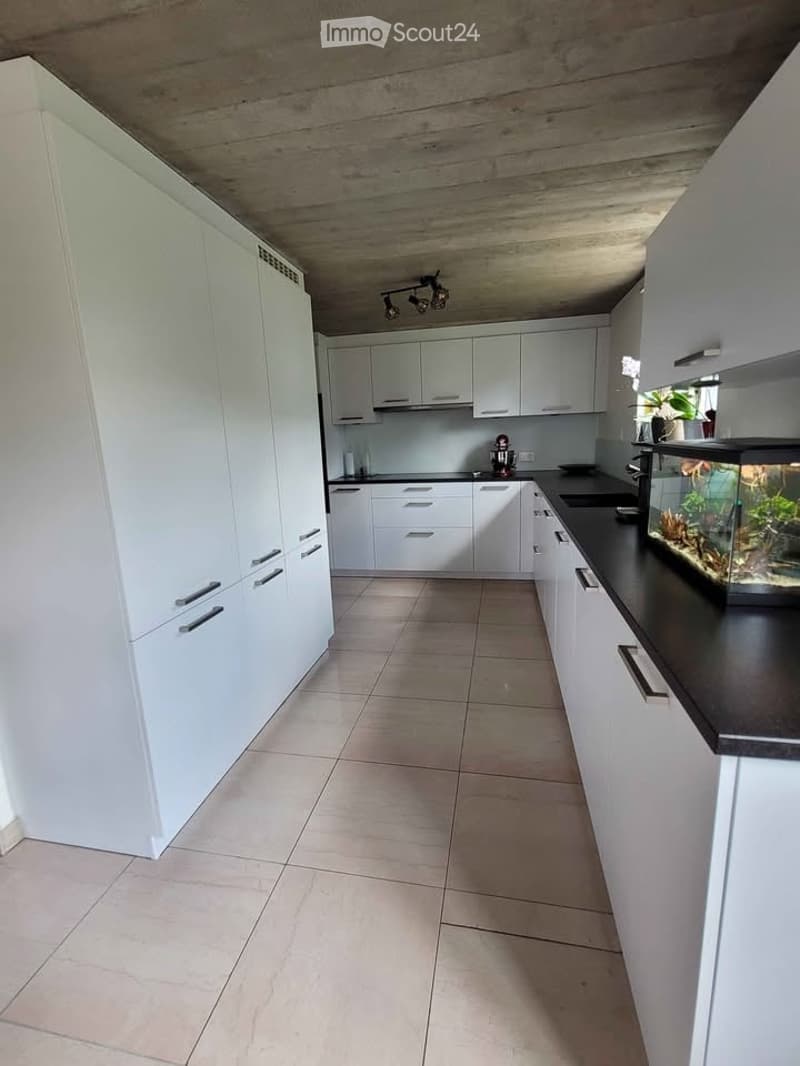 Modern kitchen with white cabinets, black countertops, tiled floor, and a fish tank on the counter.