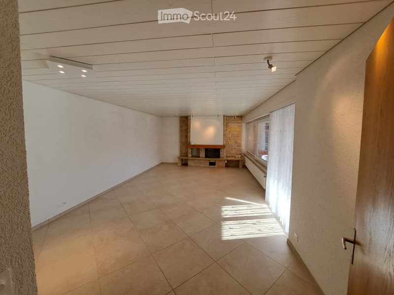 Empty room with tiled floor, white walls, and a fireplace area with a stone surround and a small bench. Natural light streams in from a window with white curtains.