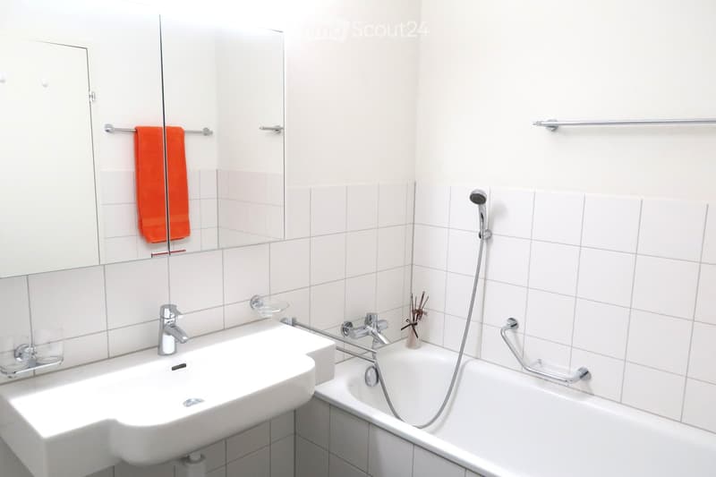 Modern bathroom with white tiles, a sink, a bathtub, a mirror, and a towel hanging on a rack.