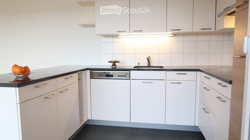 Modern kitchen with white cabinets, black countertops, a dishwasher, and a sink. A bowl of oranges is placed on the counter.