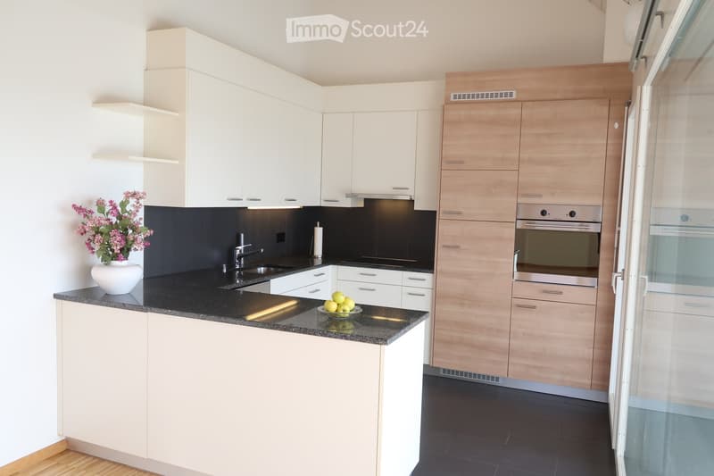 Modern kitchen with white and light wood cabinets, black countertops, stainless steel appliances, and a vase with flowers on the counter.