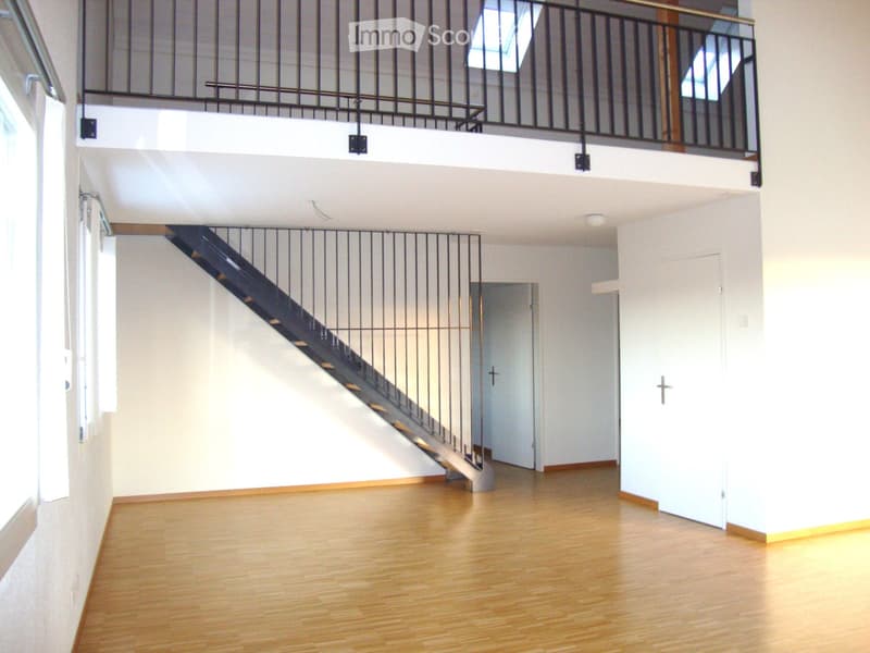 Open, modern hallway with wooden flooring, white walls, and a staircase leading to an upper level with a metal railing and skylights.