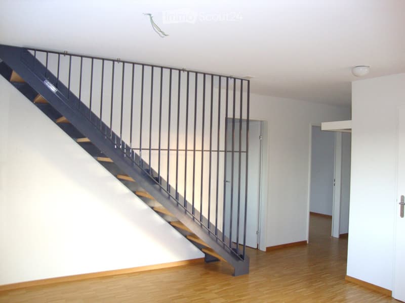 Empty hallway with wooden flooring, white walls, and a staircase with metal railing leading upwards.