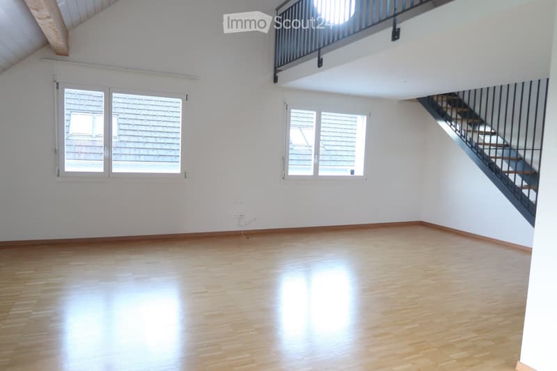 Empty room with wooden flooring, white walls, large windows, and a staircase leading to an upper level.