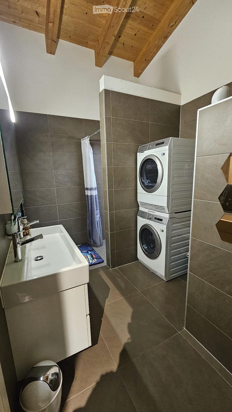 Modern bathroom with a sink, toothbrush holder, shower curtain, and a stacked washing machine and dryer unit.