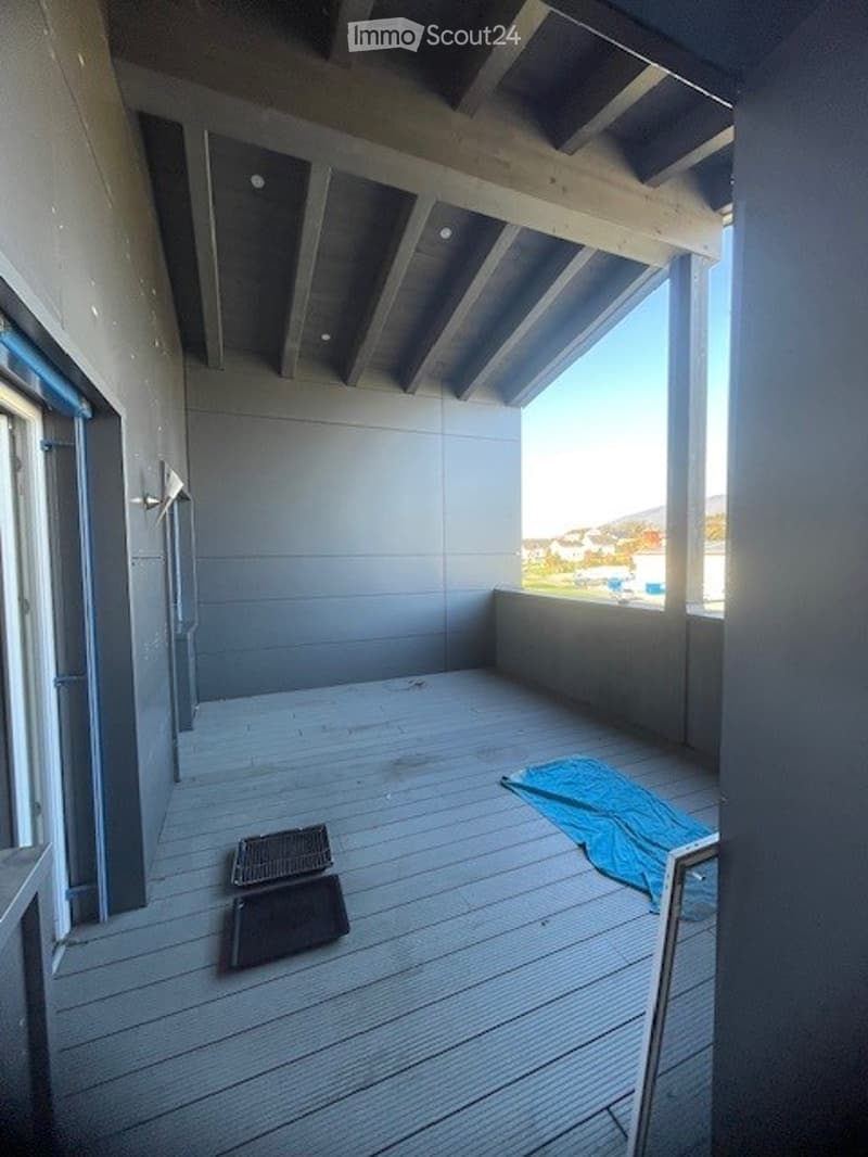 Empty wooden balcony with grey walls, open ceiling beams, and a view of the landscape.