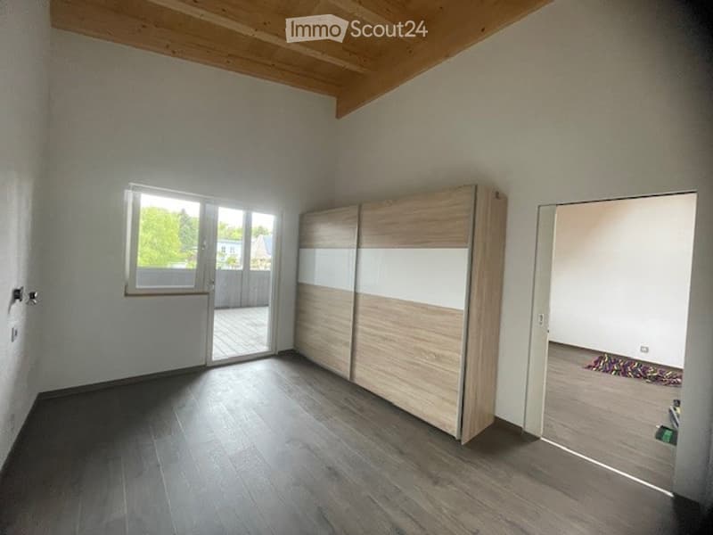 Empty room with wooden flooring, white walls, large window with sliding doors leading to a balcony, and a built-in wardrobe unit.