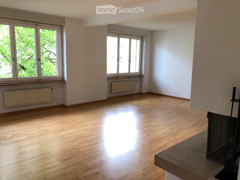 Empty room with wooden flooring, white walls, large windows, and radiators under the windows.