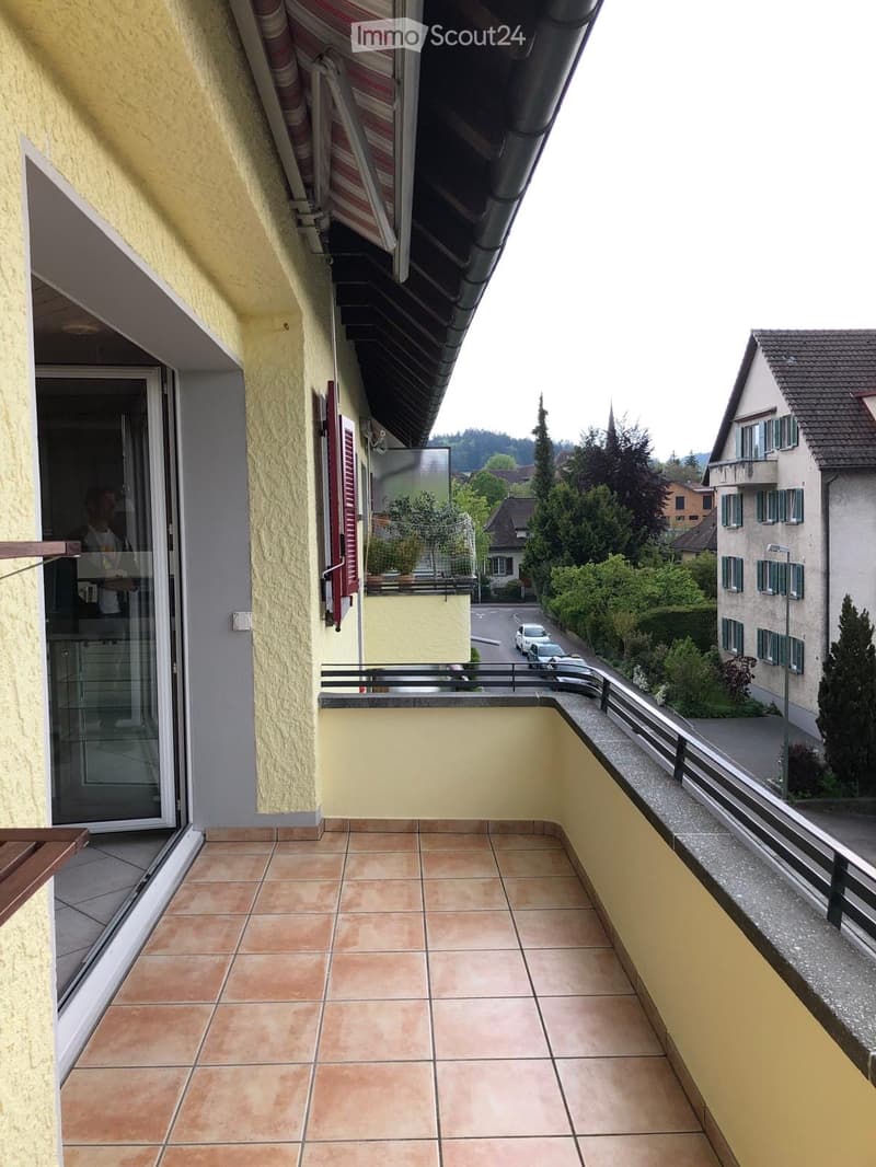 Balcony with tiled floor, glass door leading inside, metal railing, and view of street and neighboring houses.