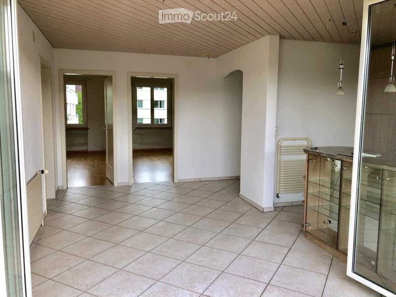 Empty hallway with tiled floor, white walls, and several doors leading to other rooms. Natural light from windows at the end of the hallway.