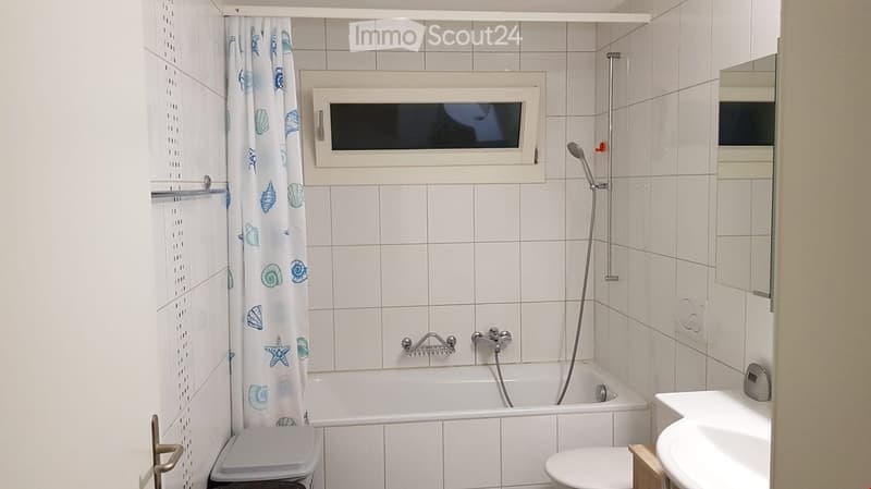 Bathroom with white tiled walls, bathtub, toilet, sink, mirror, and a showerhead with a curtain.