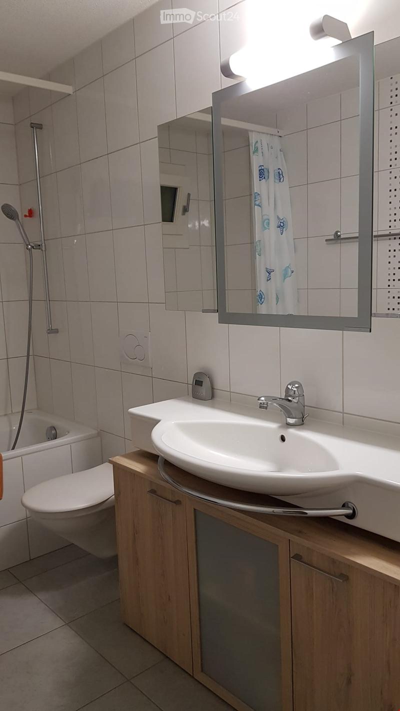 Modern bathroom with a white sink, chrome faucet, large mirror, shower area, and a toilet. Wooden cabinetry and tiled walls.