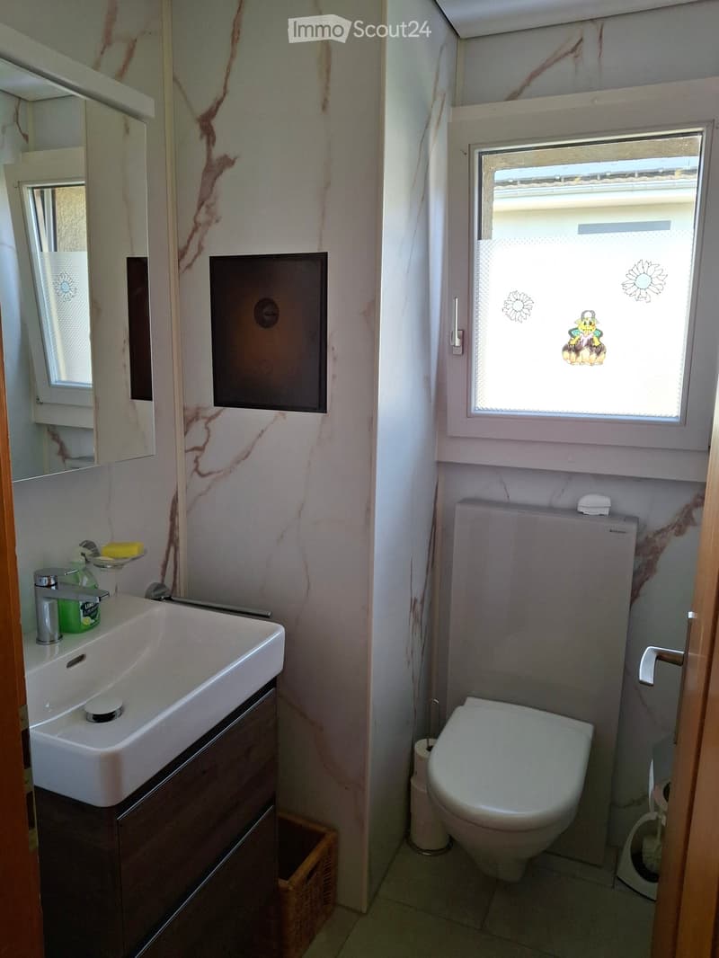 Compact bathroom with a white sink, chrome faucet, toilet, and a small window with decorative stickers. Includes a mirrored cabinet and a wooden cabinet under the sink.