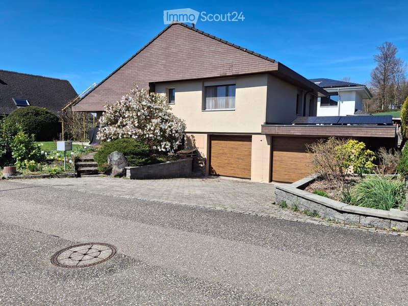 Two-story house with beige siding, brown tiled roof, two garage doors, and a landscaped front yard with steps leading to the entrance.