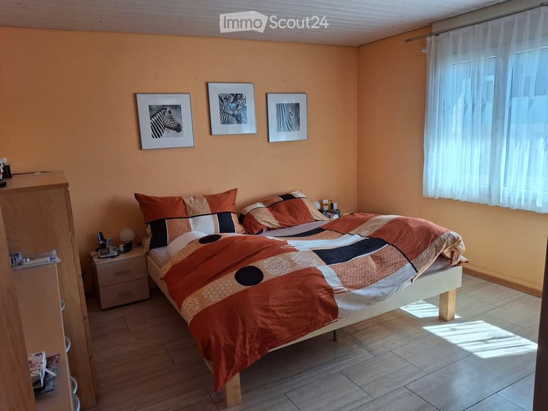 Bedroom with a double bed, orange and white bedding, nightstand, and three picture frames on the wall.
